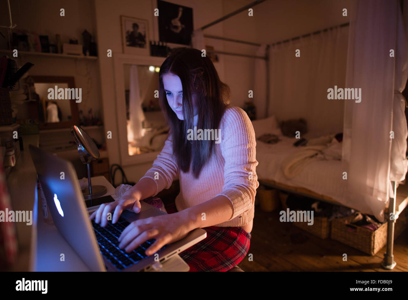 A 17 year old teenage girl on her Apple laptop computer in her bedroom at night, checking her Facebook page and sending messages to her friends, UK Stock Photo