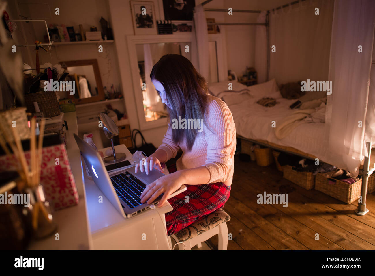 A 17 year old teenage girl on her Apple laptop computer in her bedroom at night, checking her Facebook page and sending messages to her friends, UK Stock Photo