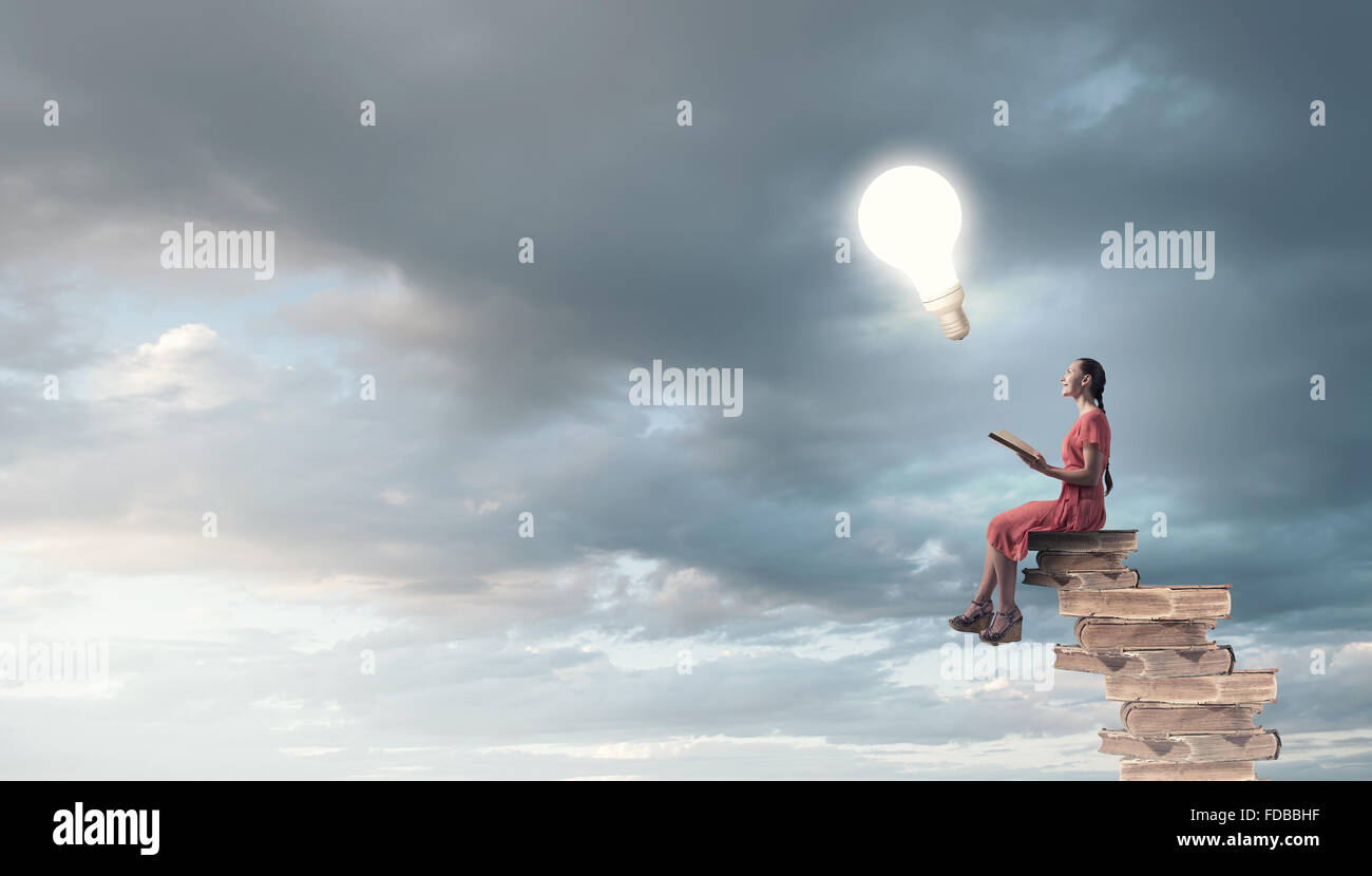 Young girl sitting on stack of books and reading Stock Photo - Alamy