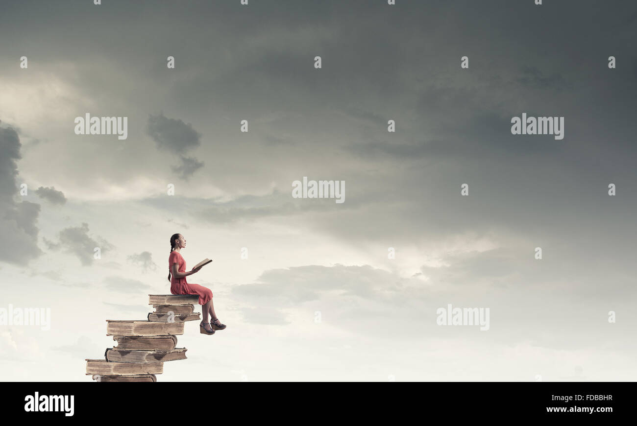 Young girl sitting on stack of books and reading Stock Photo - Alamy