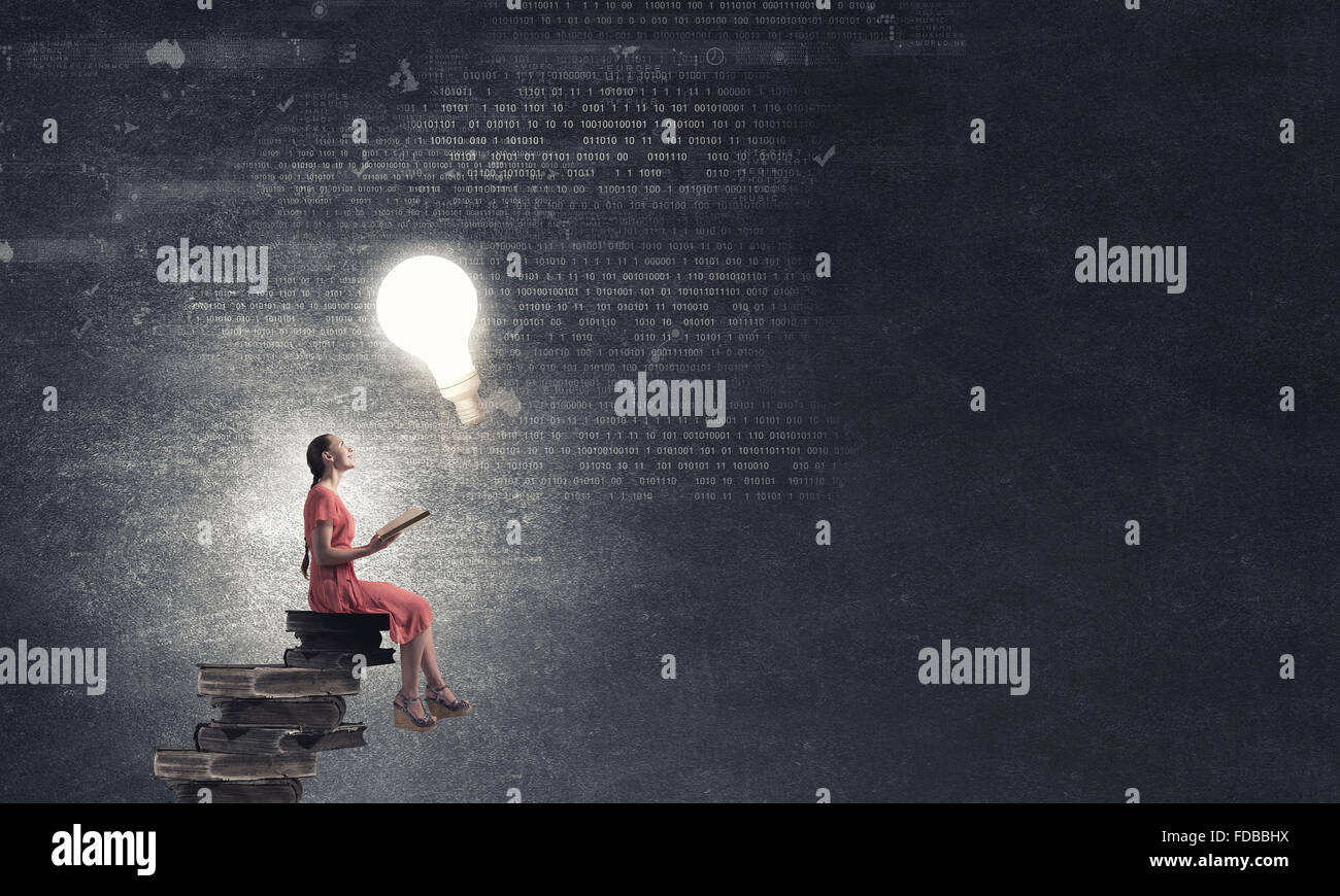 Young girl sitting on stack of books and reading Stock Photo - Alamy