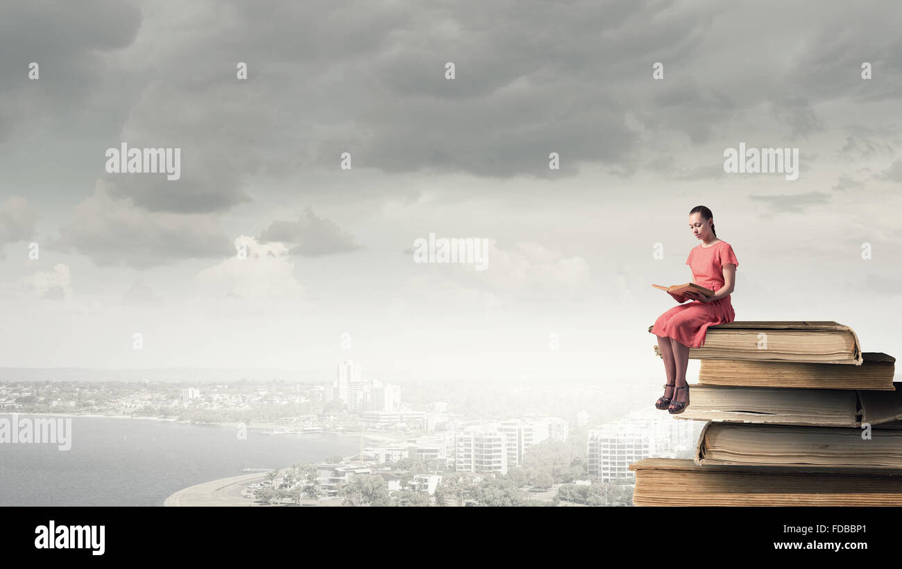 Young girl sitting on stack of books and reading Stock Photo - Alamy