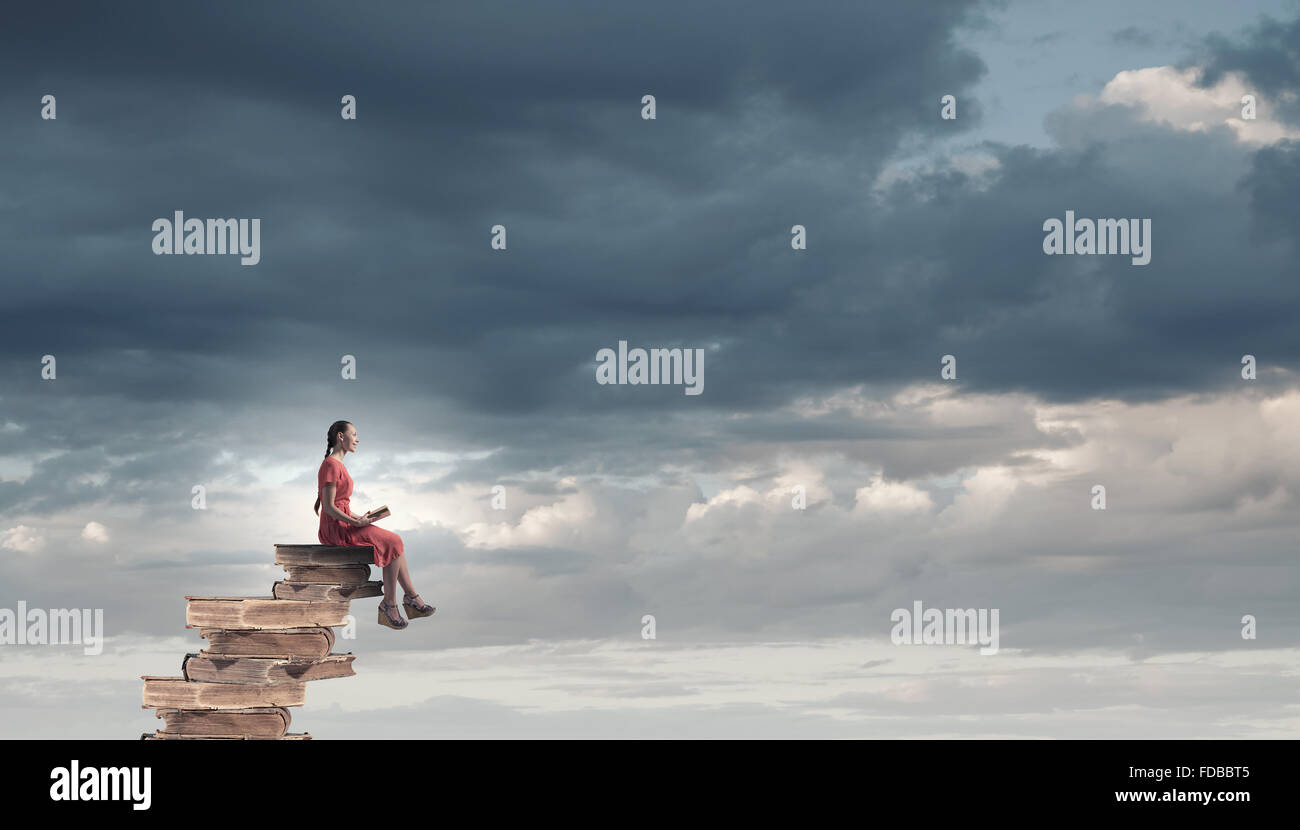 Young girl sitting on stack of books and reading Stock Photo - Alamy