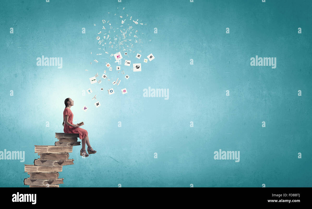 Young girl sitting on stack of books and reading Stock Photo - Alamy