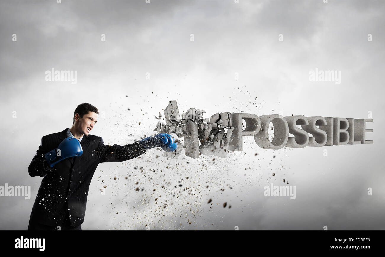 Young businessman in blue boxing gloves breaking impossible word Stock