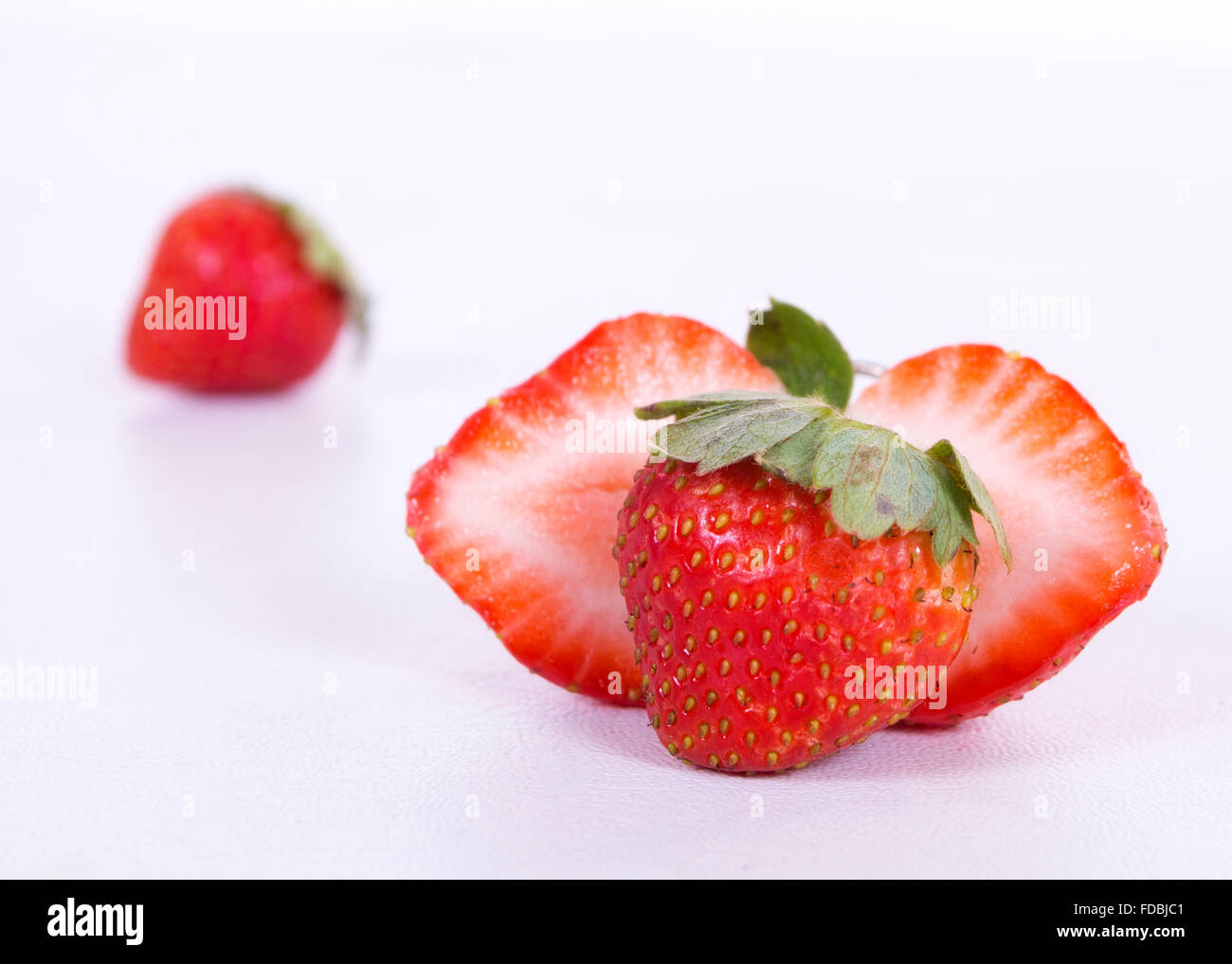 a whole strawberry in the foreground, behind a chopped in half and another distant strawberry Stock Photo