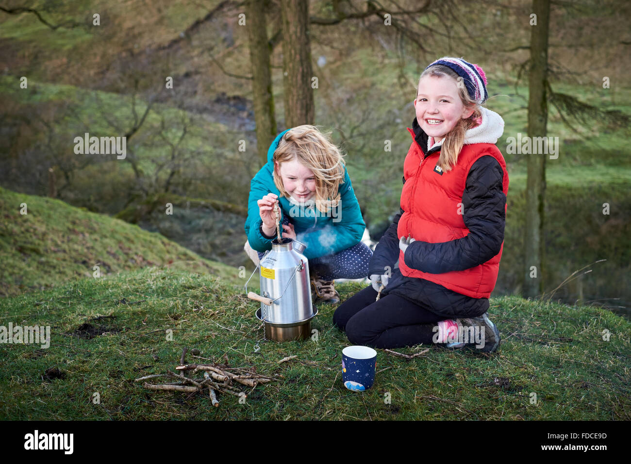Two girls using a Kelly Kettle stove to cook outdoors smiling and