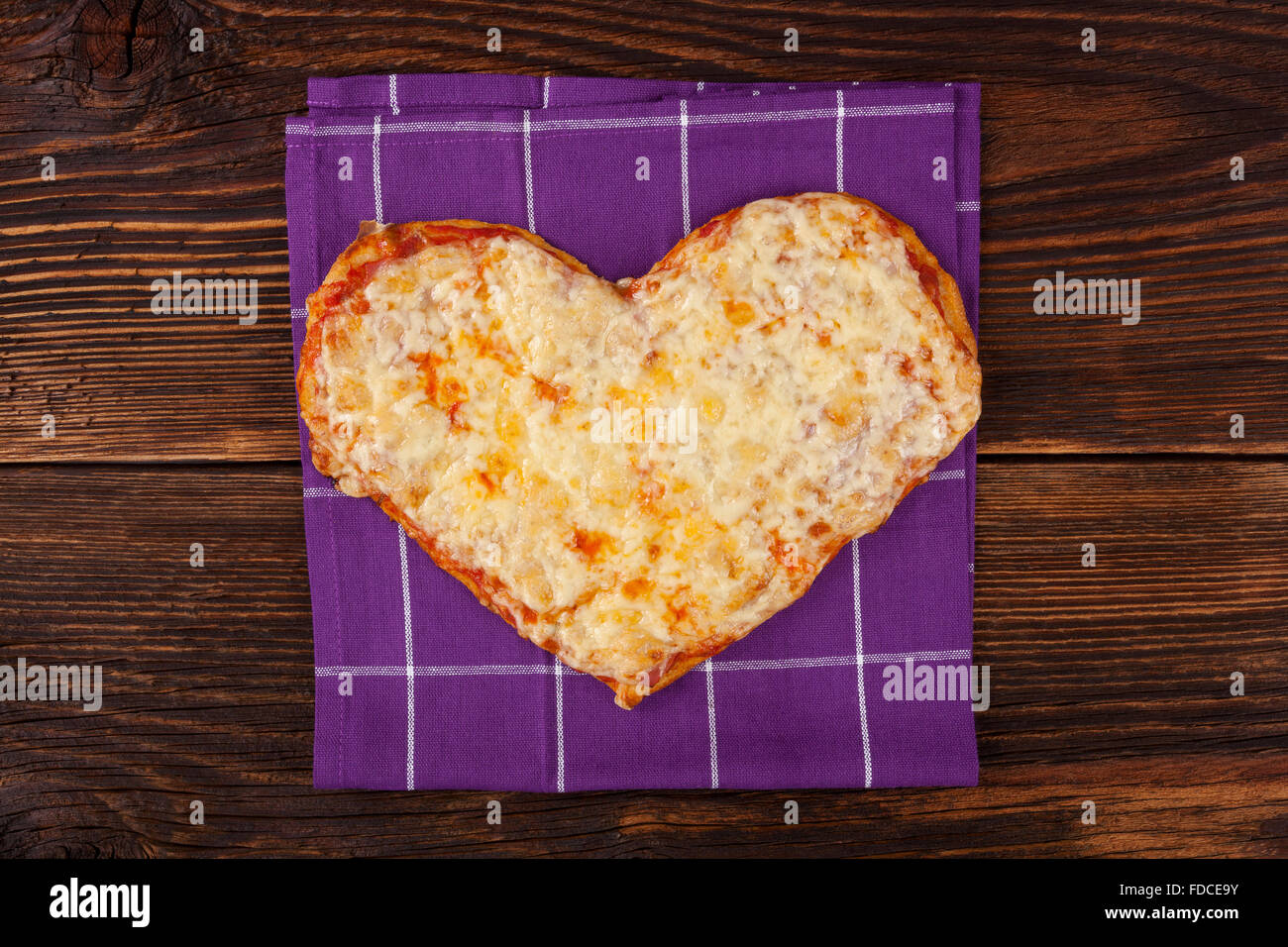 Delicious pizza in heart shape on wooden table, top view. Culinary pizza eating. Stock Photo