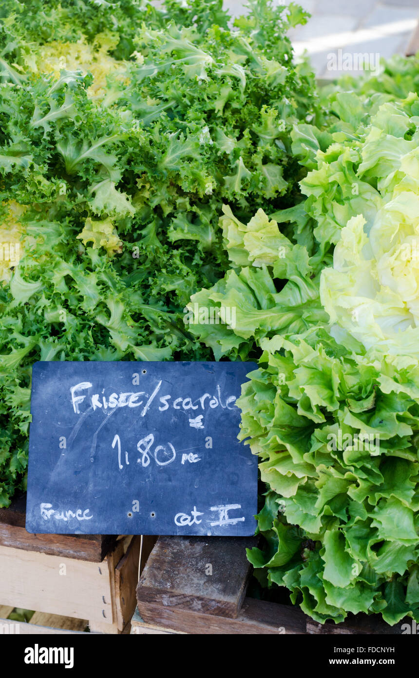 Frisee/scarole; leafy green salad vegetable displayed on a French farmer's market stall in wooden box with chalkboard price tag Stock Photo