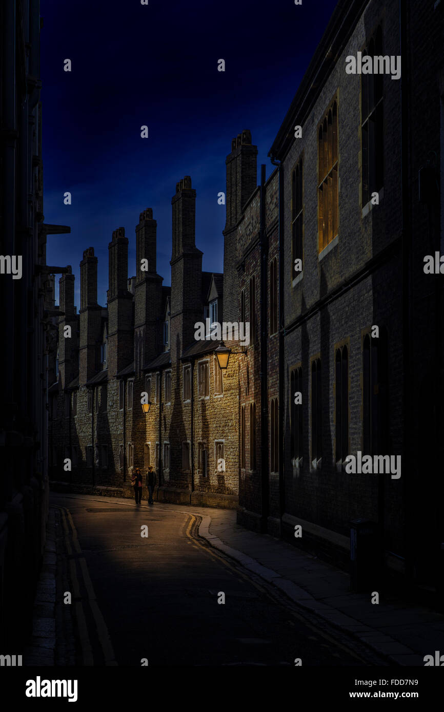 Night street scene in Cambridge showing row of chimneys with two people walking under the lamp light  United Kingdom Stock Photo