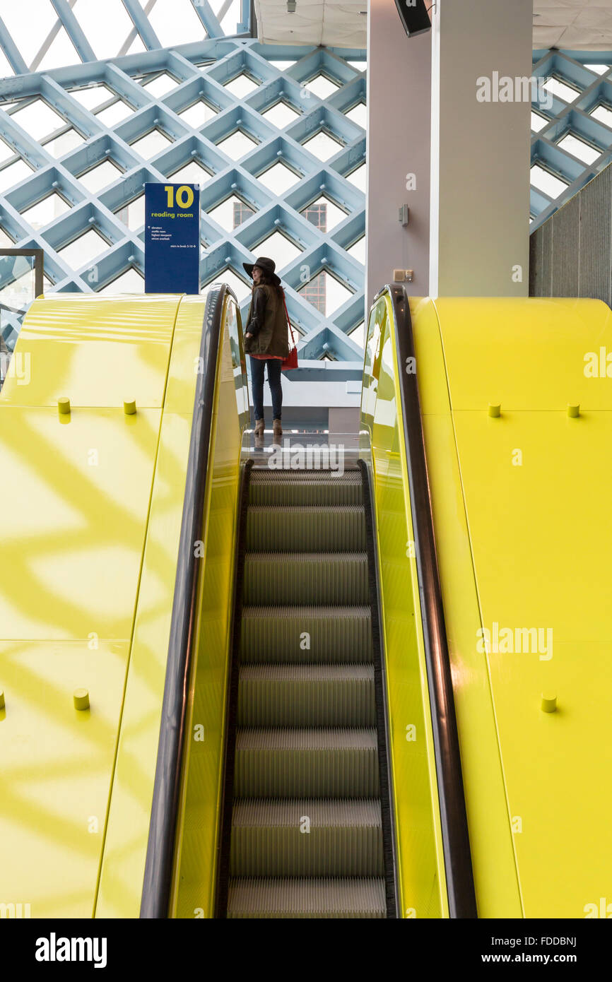 Woman at top of escalator in the modern Seattle Central Library, designed by architects Rem Koolhaas and Joshua Prince-Ramus Stock Photo