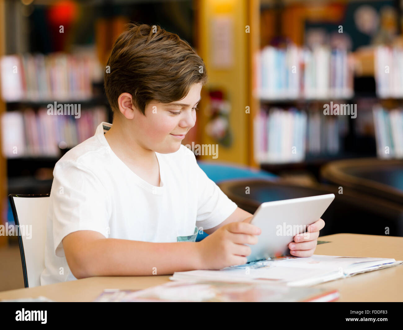 Teenage boy sitting with tablet in library Stock Photo - Alamy