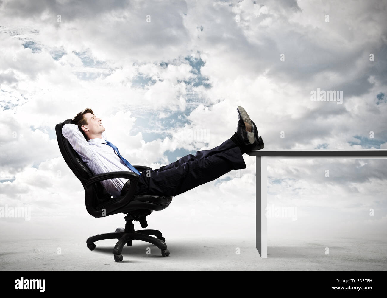 Smiling businessman sitting in chair with legs on table Stock Photo - Alamy