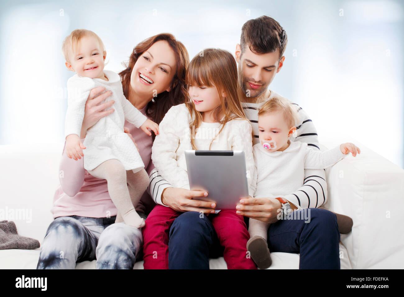 Portrait of happy family with twins and little daugther sitting at sofa. Stock Photo