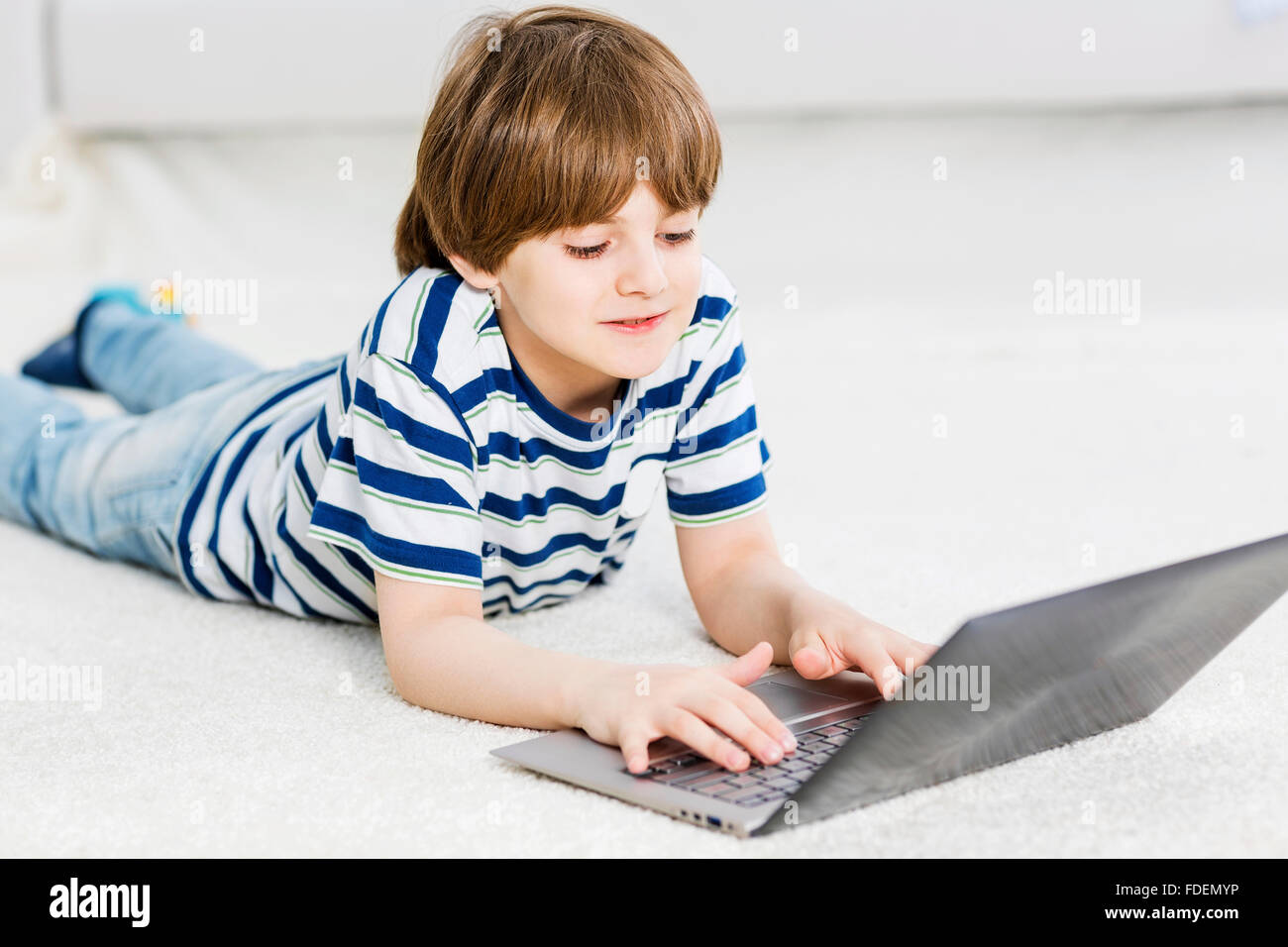 Cute boy lying on floor and using laptop Stock Photo - Alamy