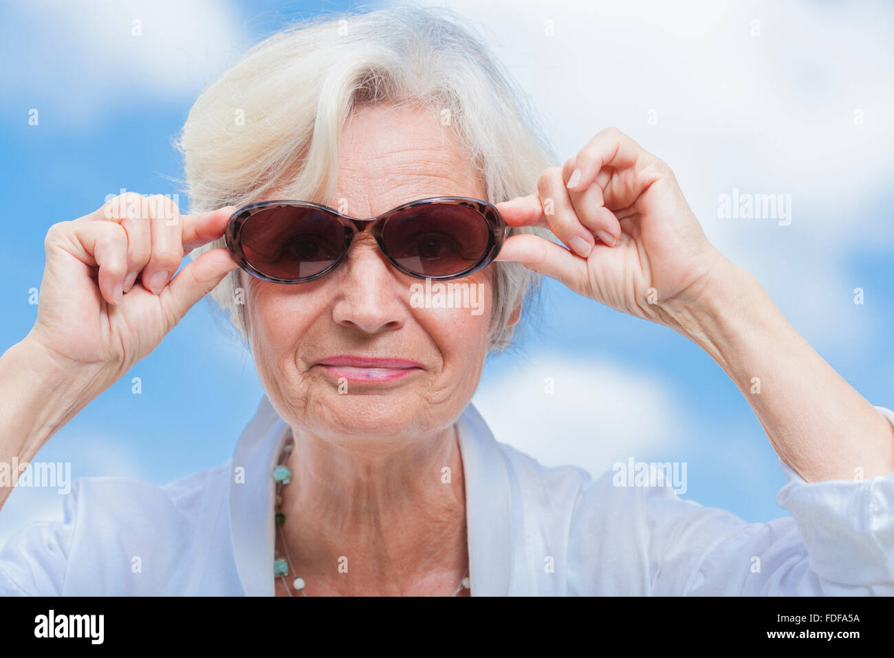 senior old woman smiling with sunglasses in front of blue summer sky ...