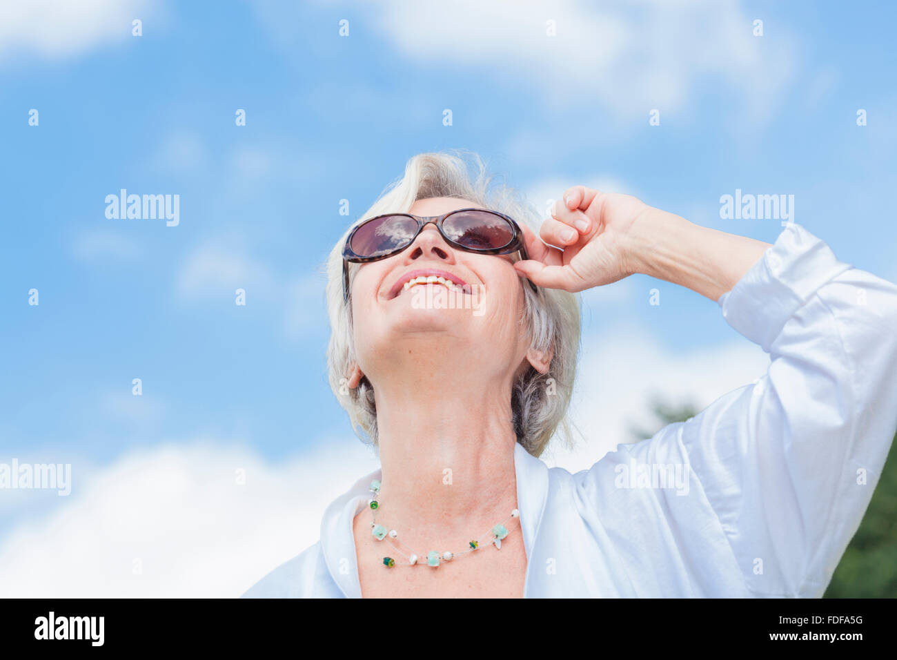 senior old woman smiling with sunglasses in front of blue summer sky ...