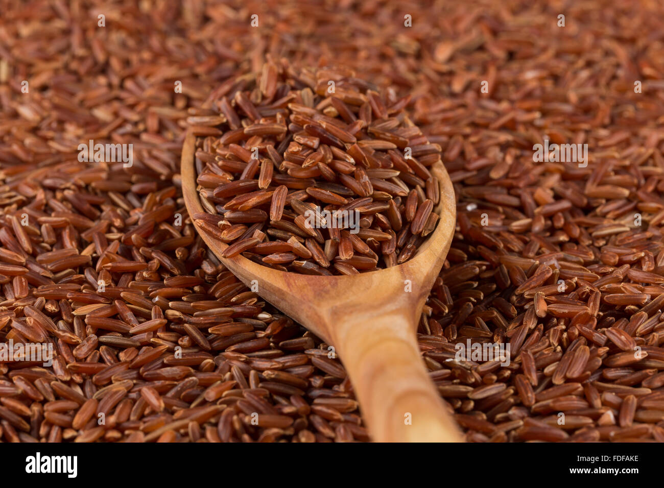 Red rice in a wooden spoon on red rice background Stock Photo - Alamy