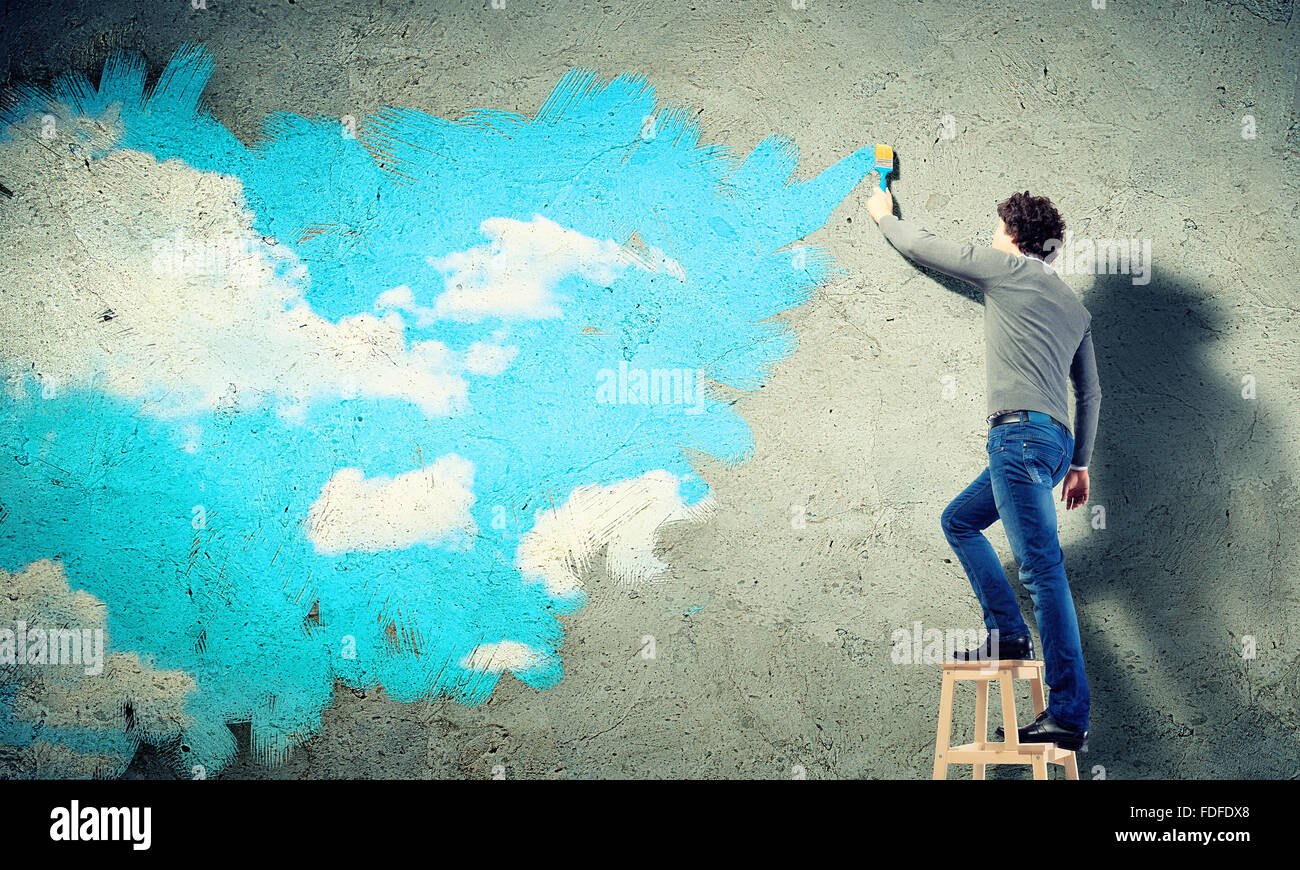 Young man drawing a cloudy blue sky on the wall Stock Photo - Alamy