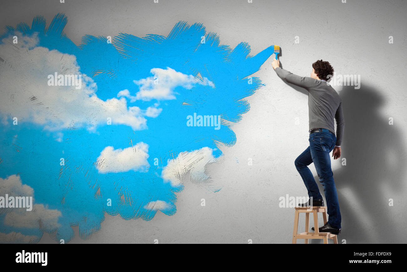 Young man drawing a cloudy blue sky on the wall Stock Photo - Alamy