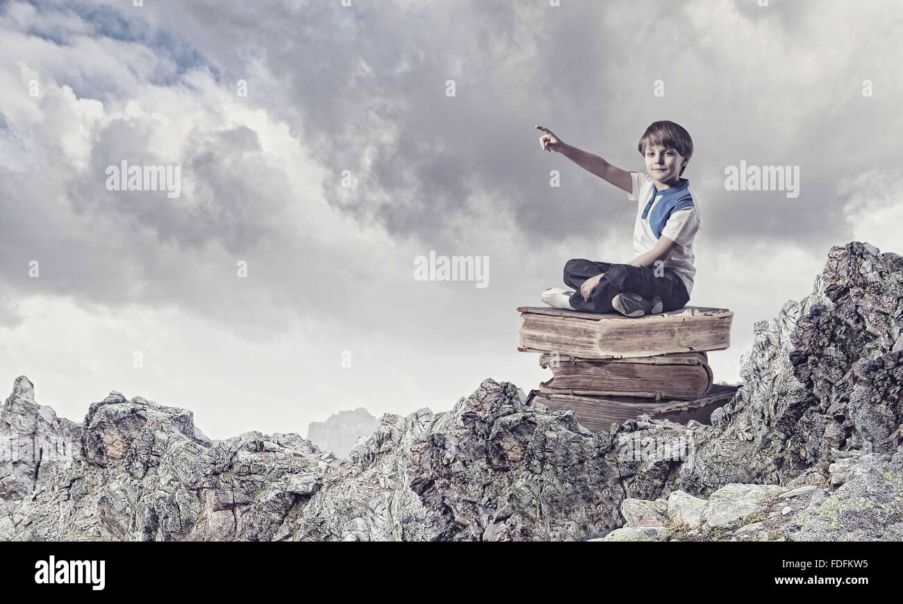 Image of little cute boy sitting on pile of books Stock Photo - Alamy