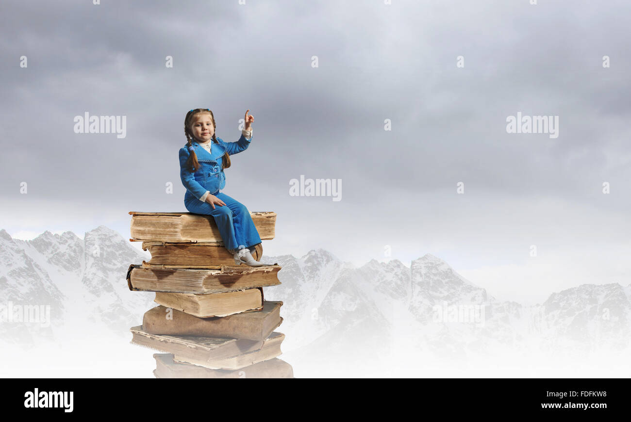 Image of cute school girl in sitting on pile of books Stock Photo - Alamy