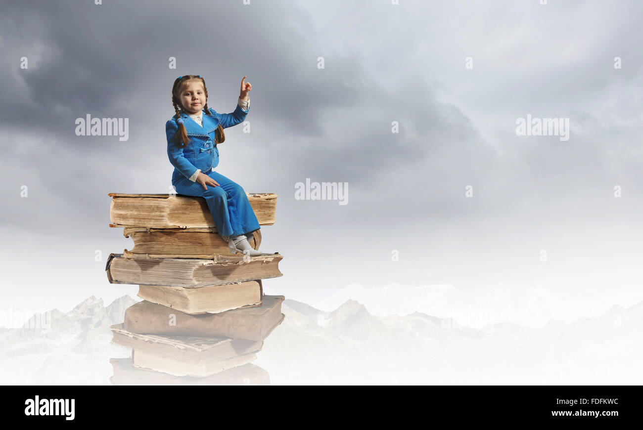 Image of cute school girl in sitting on pile of books Stock Photo - Alamy