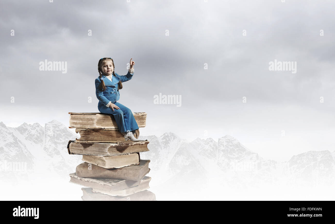 Image of cute school girl in sitting on pile of books Stock Photo - Alamy