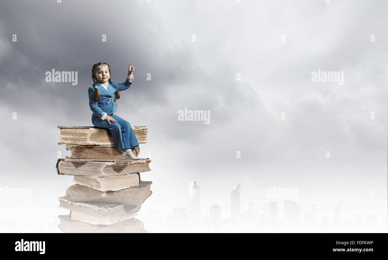 Image of cute school girl in sitting on pile of books Stock Photo - Alamy
