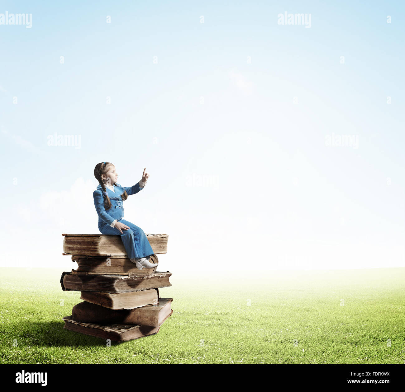 Image of cute school girl in sitting on pile of books Stock Photo - Alamy