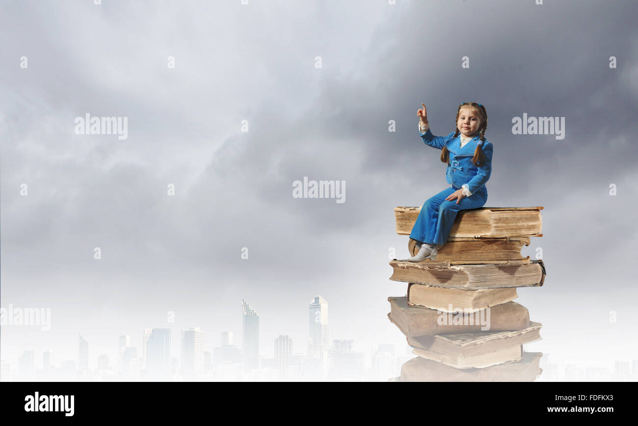 Image of cute school girl in sitting on pile of books Stock Photo - Alamy
