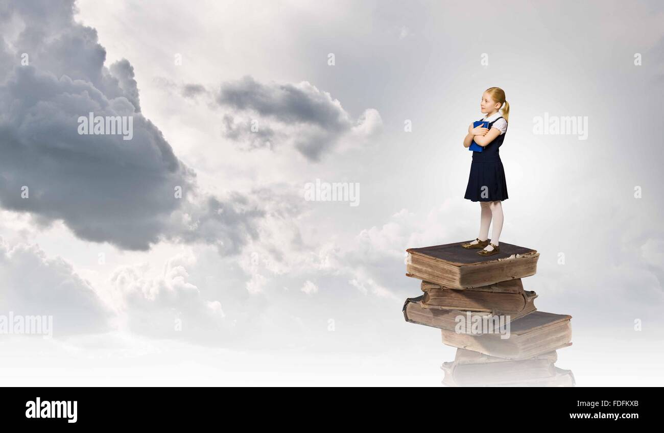 Image of cute school girl standing on pile of books Stock Photo - Alamy