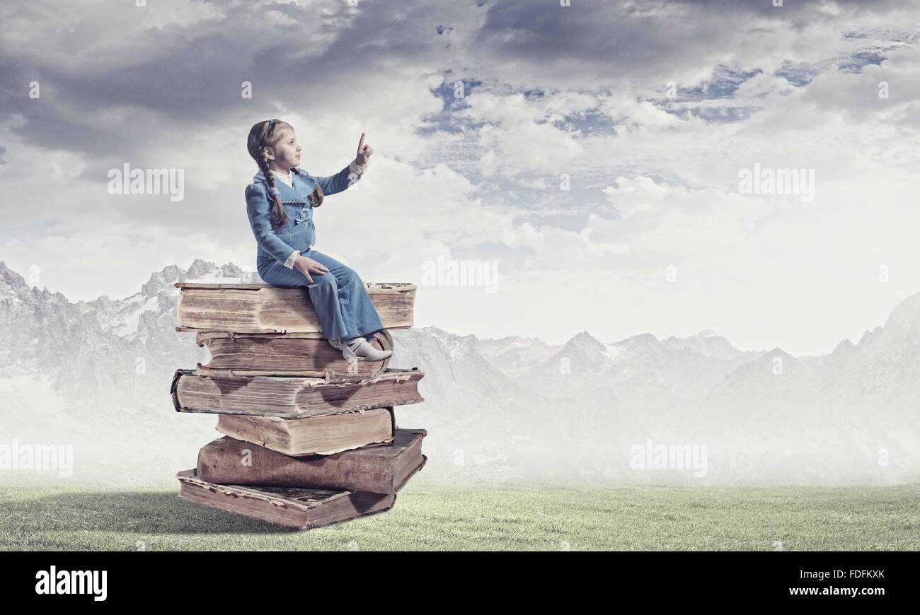 Image of cute school girl in sitting on pile of books Stock Photo - Alamy