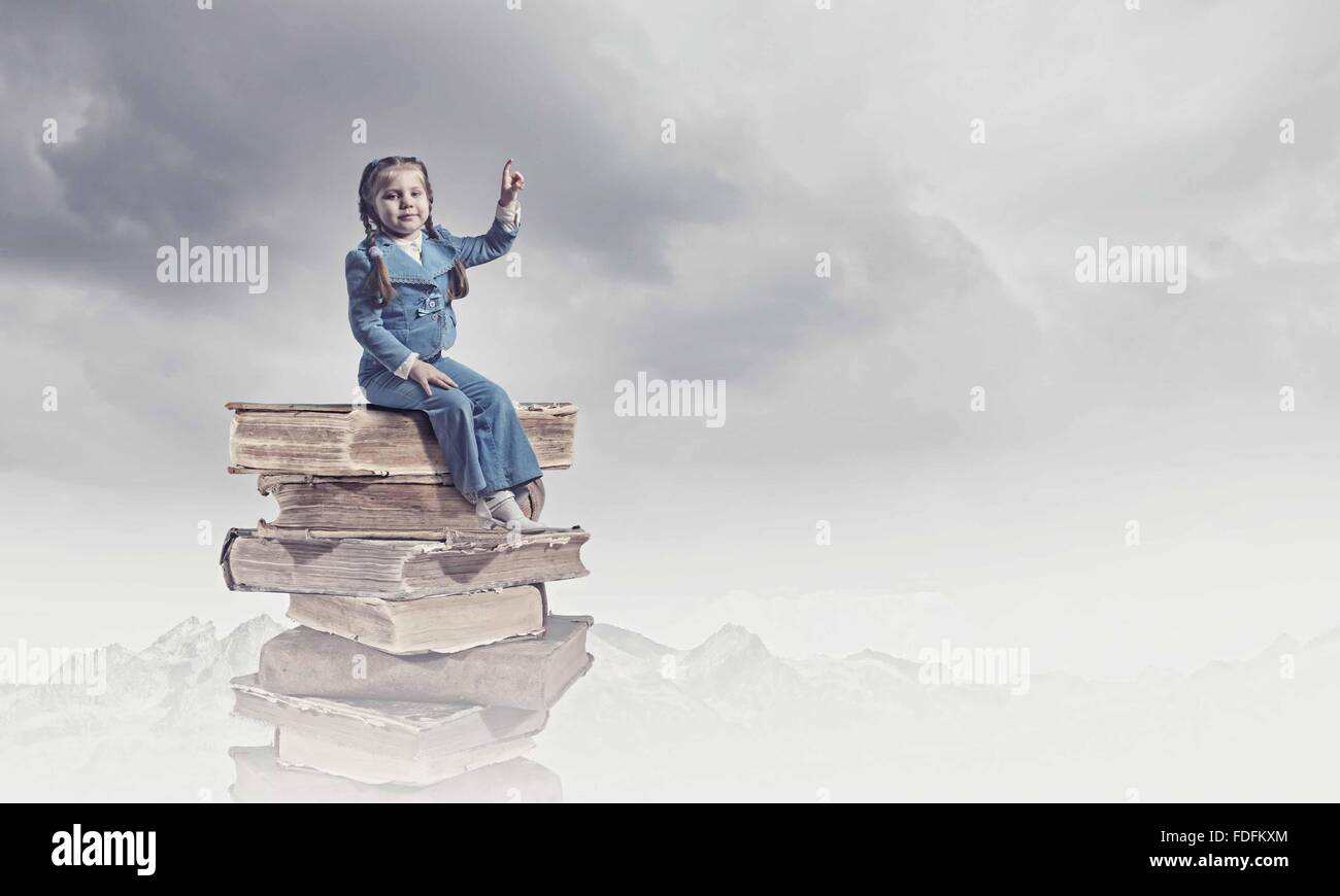 Image of cute school girl in sitting on pile of books Stock Photo - Alamy