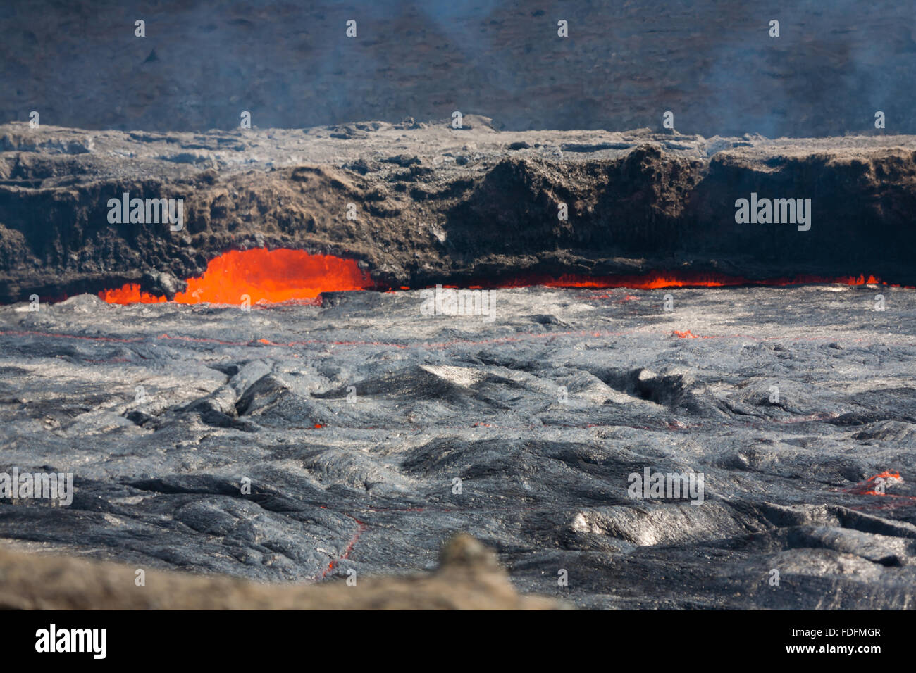 A thin crust of cooled lava moves slowly across the lava lake of Erta Ale volcano in Ethiopia. Molten rock splashes around the edges, melting a small cave. Stock Photo