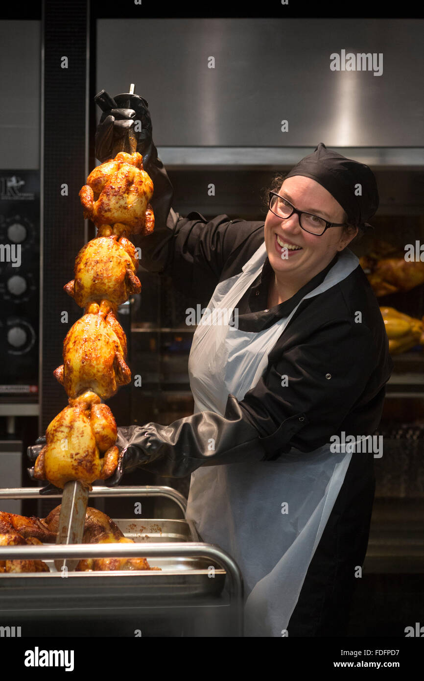 Smiling employee in a chicken rotisserie (France). Spit roasted chickens. Female, working, work. Stock Photo