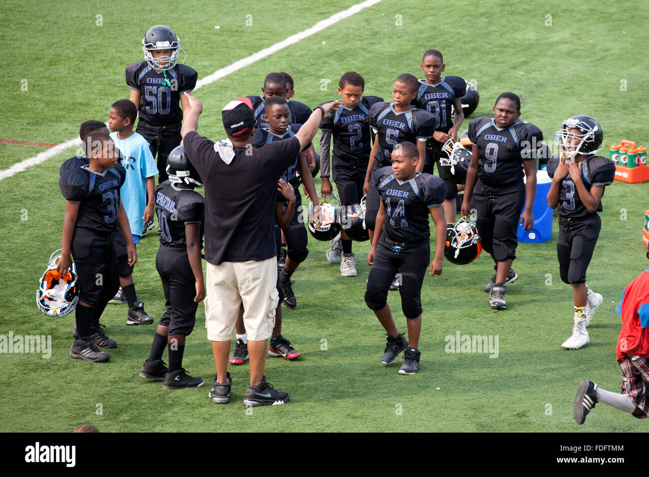 Black football team age 12 and coach instructing his players on the field. St Paul Minnesota MN USA Stock Photo
