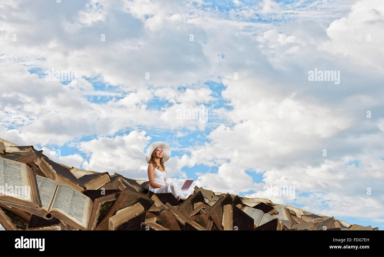Young lady sitting on pile of books with laptop Stock Photo - Alamy
