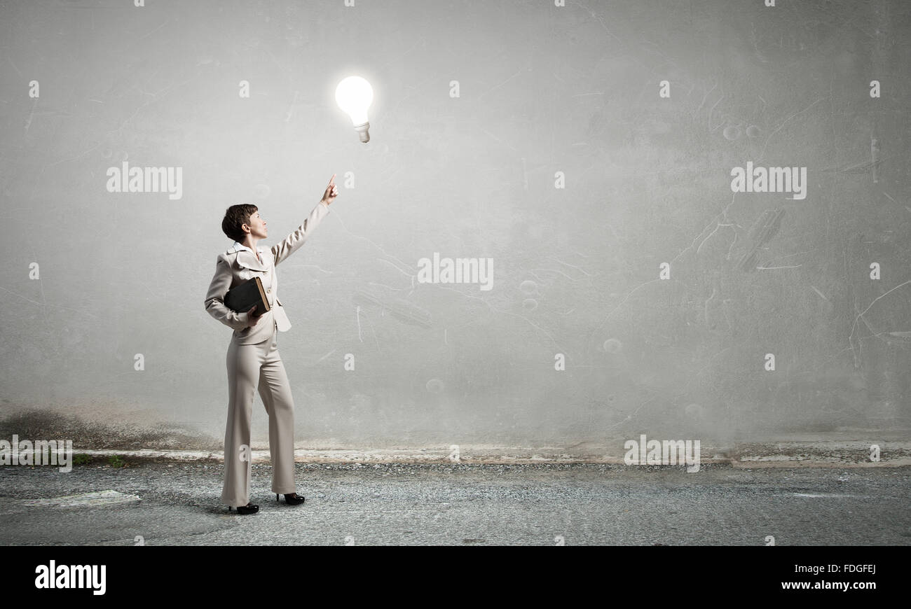 Adult woman in suit with old book in hand pointing at light bulb Stock Photo