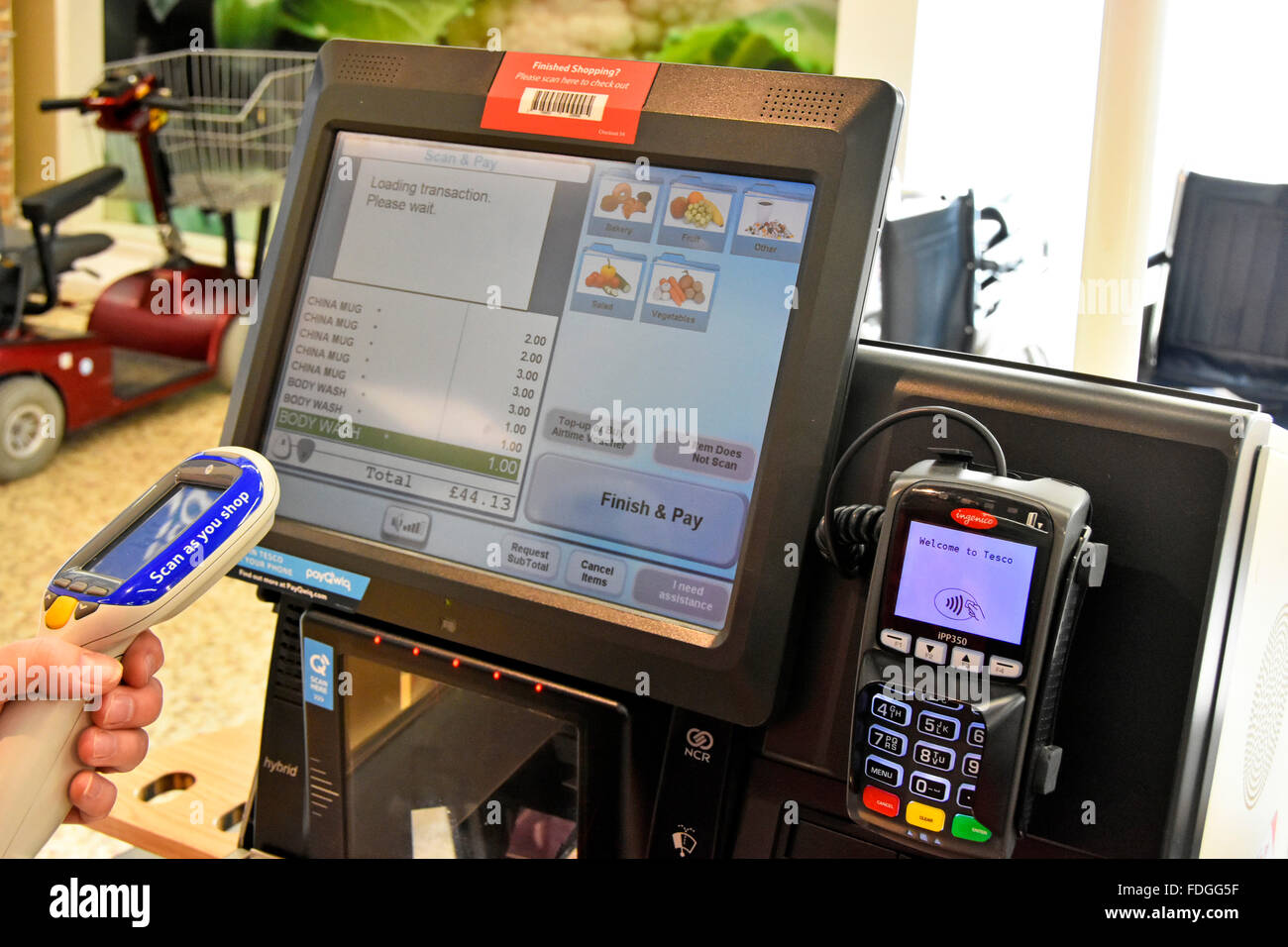 Tesco shopper aiming her Scan as you shop device to upload shopping items onto screen for payment at self service checkout till in London England UK Stock Photo