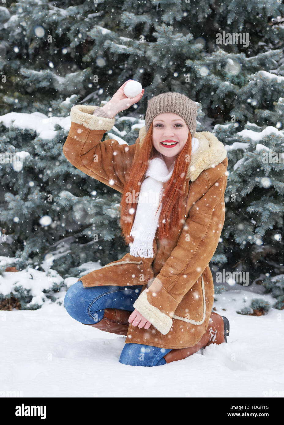 Girl play snowballs in winter park at day. Snowy fir trees. Redhead woman full length. Stock Photo