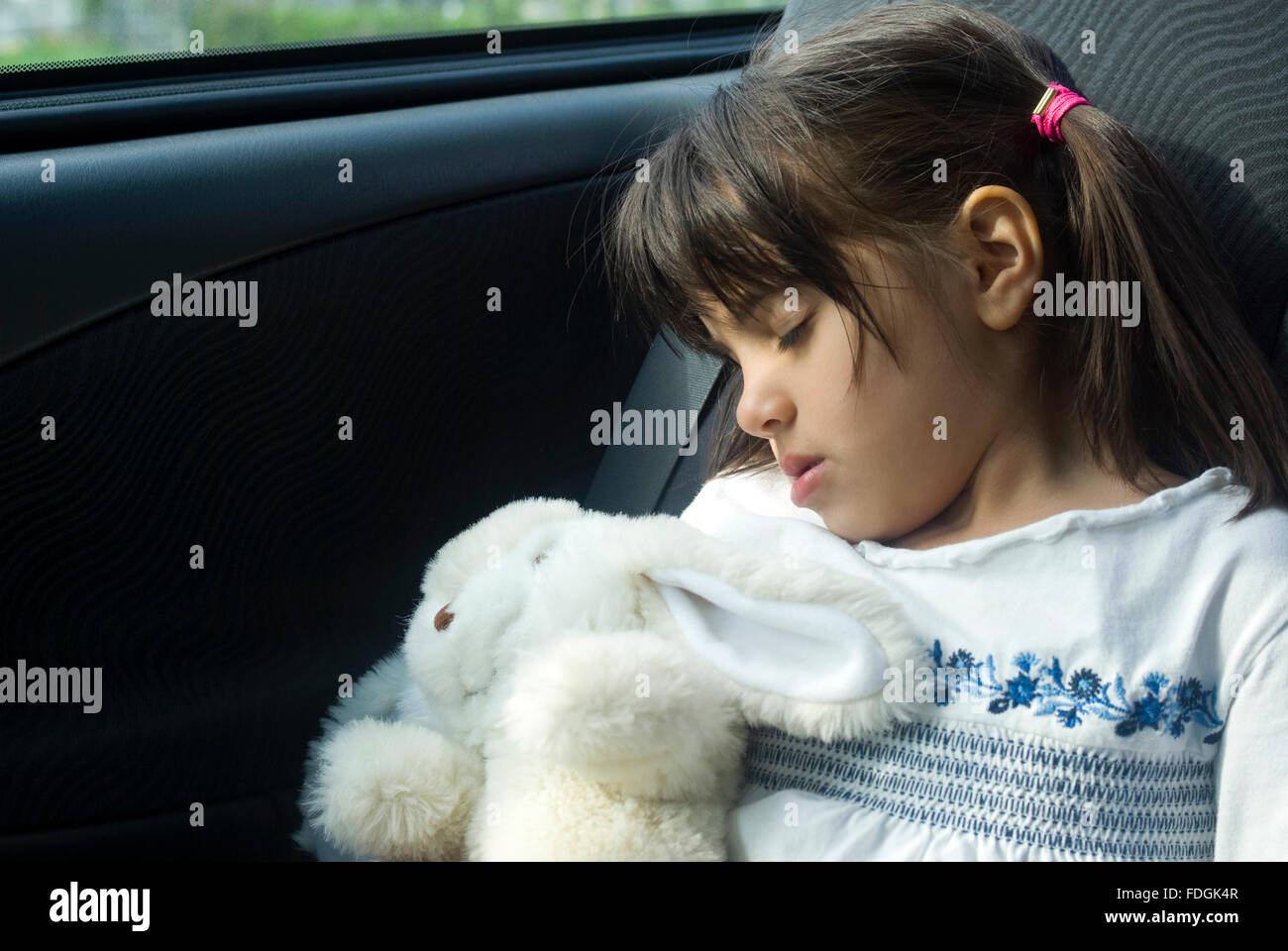 Girl sleeping at back seat of car hugging at his soft toy Stock Photo