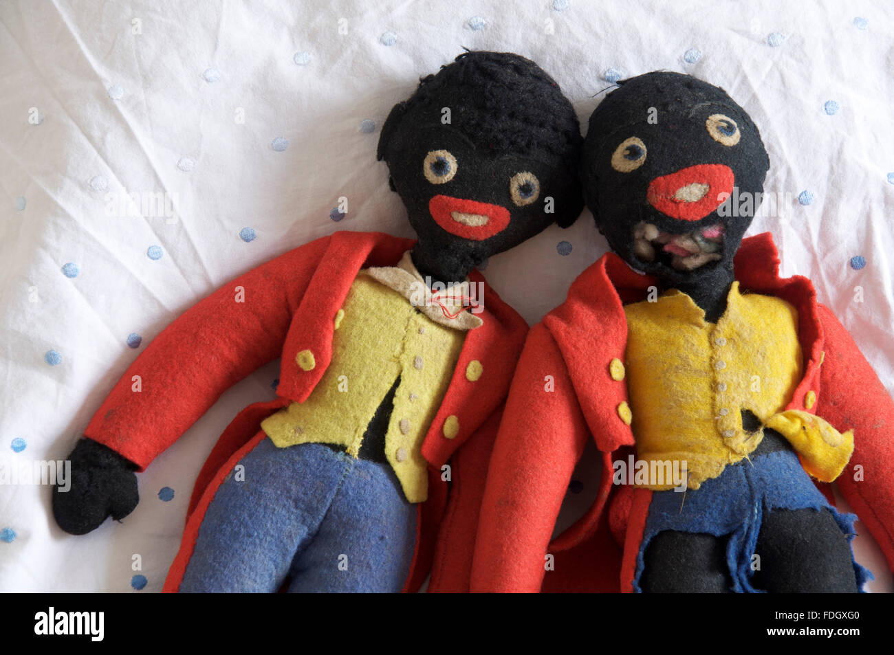 Two old well worn and much loved golliwog dolls lying together on a white bedsheet. Stock Photo