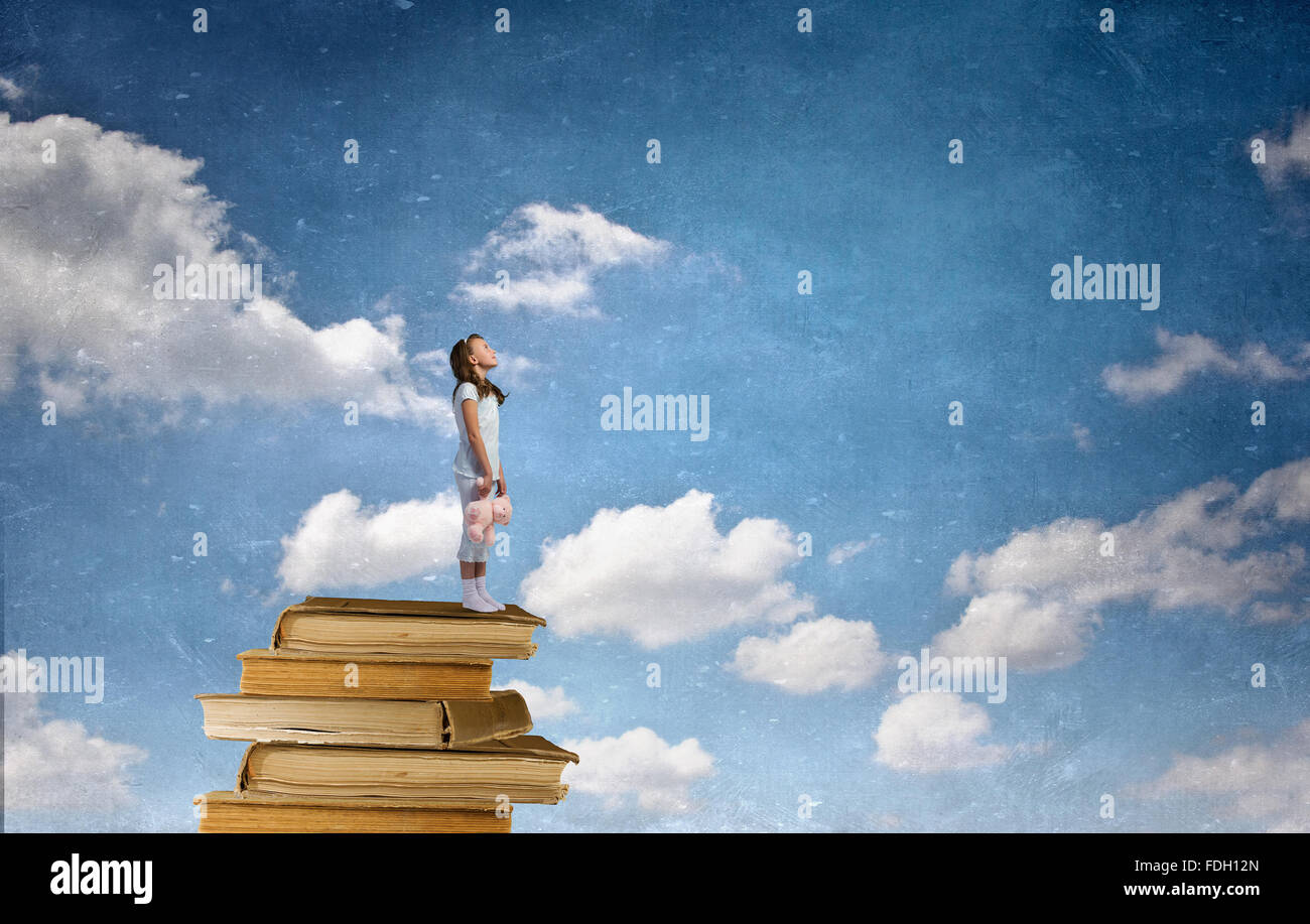 Cute girl wearing pajamas with toy bear in hand standing on pile of ...