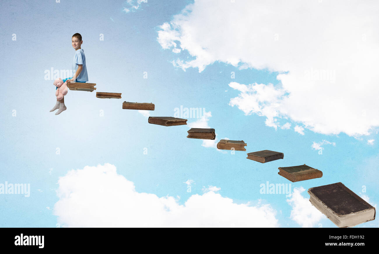 Cute little boy with toy bear sitting on ladder of books Stock Photo ...