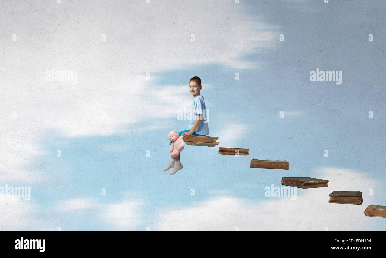 Cute little boy with toy bear sitting on ladder of books Stock Photo ...