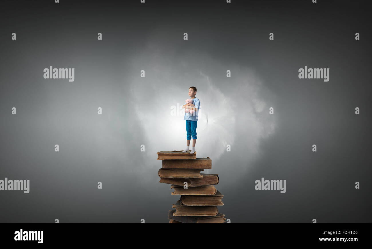 Cute little boy with toy bear standing on pile of books Stock Photo - Alamy