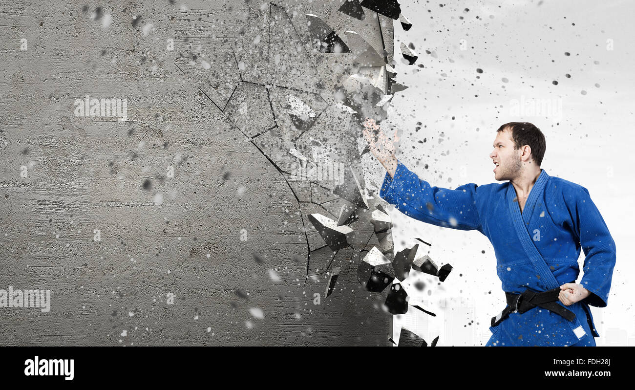 Young determined karate man breaking with hand concrete wall Stock Photo