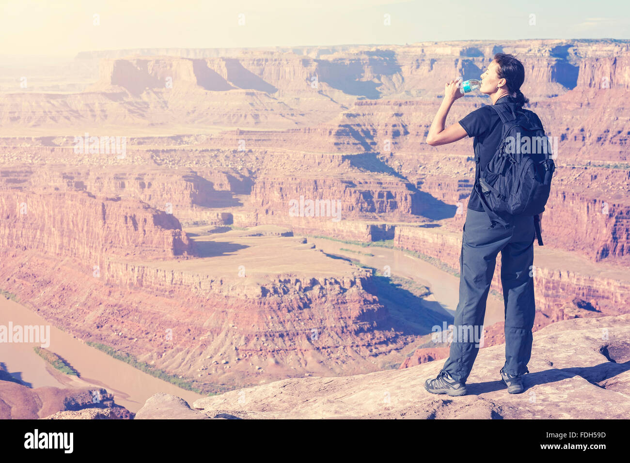 Retro toned female tourist drinking water by canyon, USA. Stock Photo