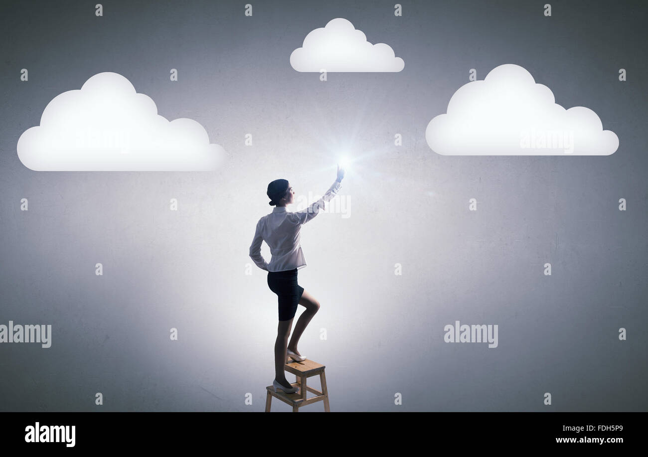 Businesswoman standing on chair and reaching cloud in sky Stock Photo ...